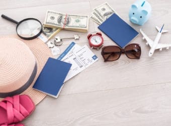 Pink piggy bank, straw hat, money, passport and sunglasses on wooden table