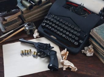 Writing a crime fiction book old retro vintage typewriter and revolver gun with ammunitions, books, papers, old ink pen